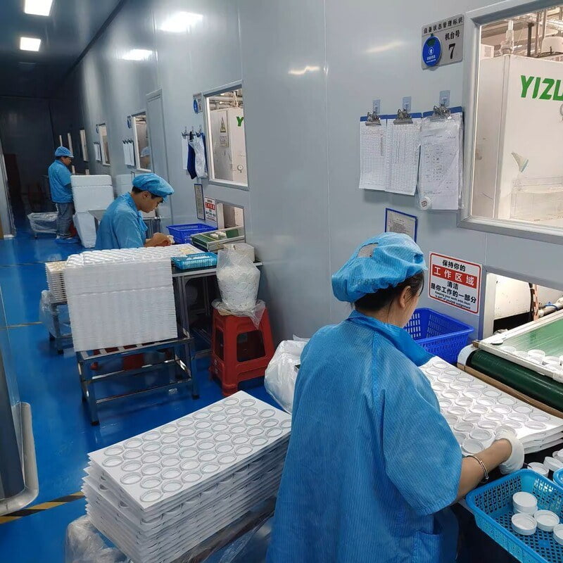 Factory staff handling cosmetic packaging components on trays