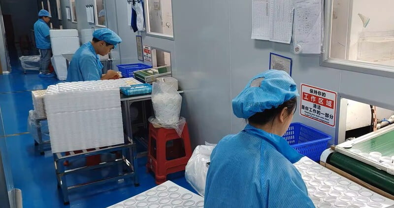 Workers handling cosmetic packaging components at factory workstations