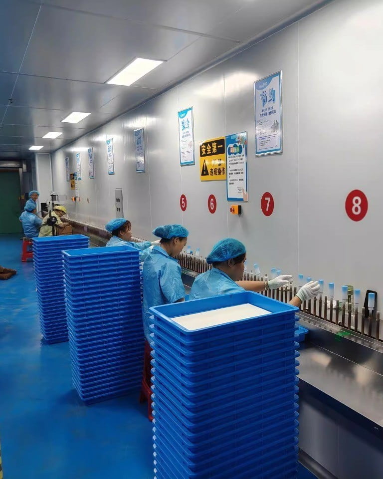 Workers inspecting cosmetic packaging components beside blue storage bins